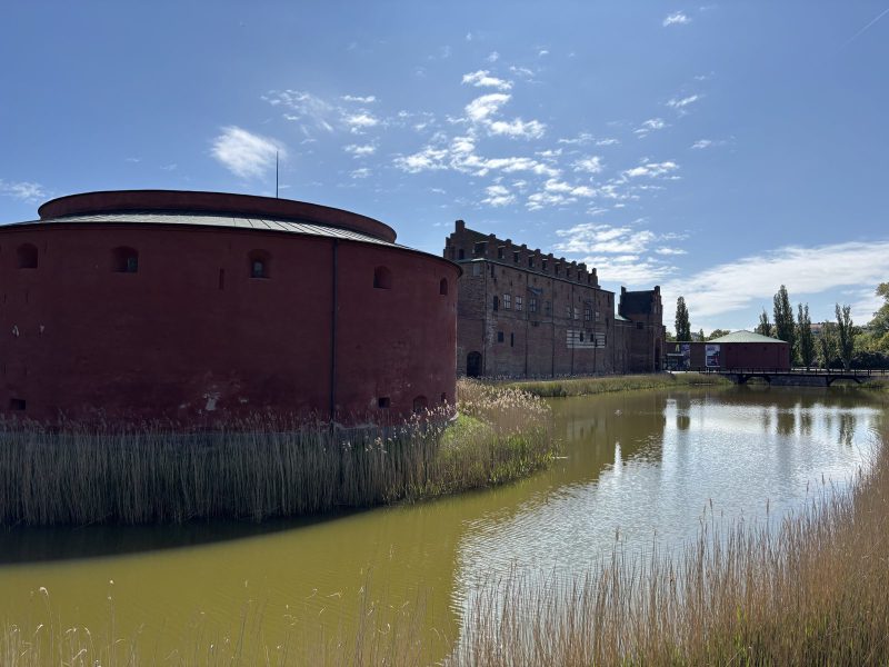 Malmöhus 的紅色圓砲塔,泡在長滿蘆葦的護城河裡。