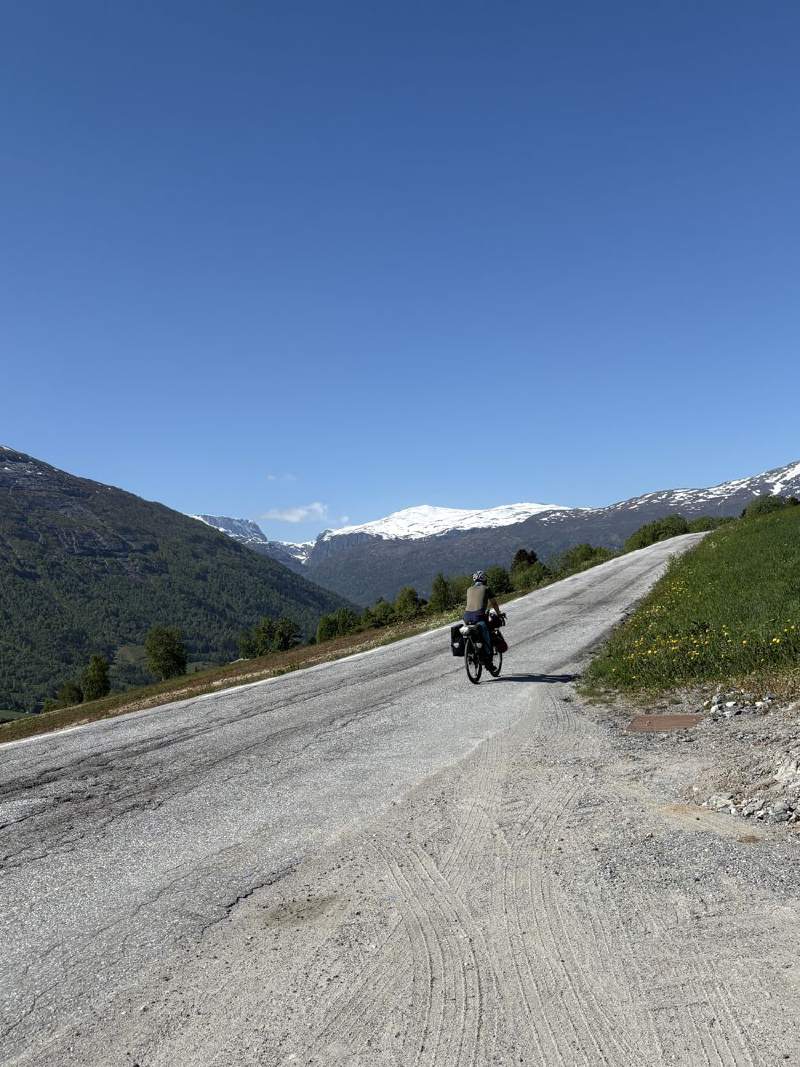 公路往遠處的雪山延伸,遠處有騎車的人。