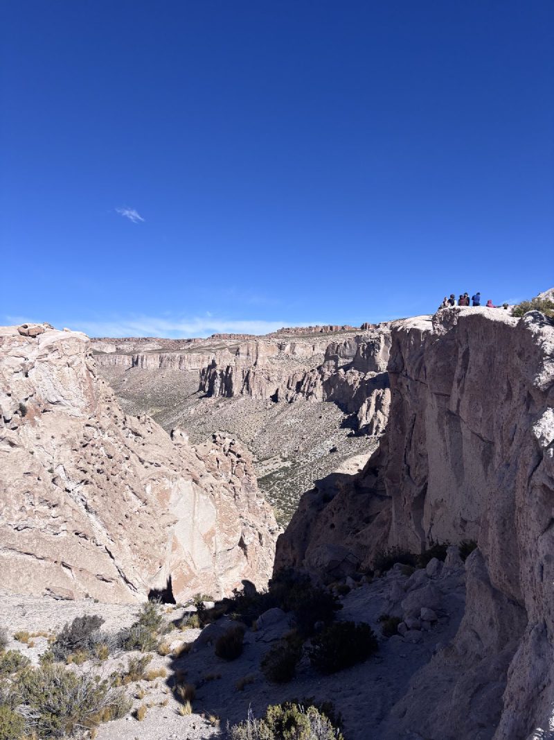 高原上的峽谷,水平層理一層一層;右邊崖上站著幾個人。