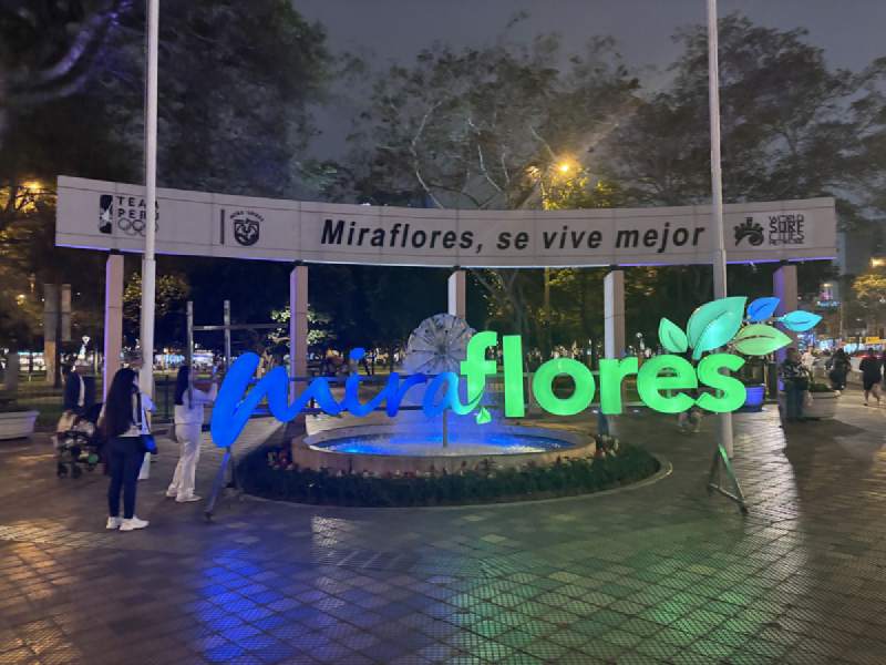 18:23,晚上,拱門上寫著「Miraflores, se vive mejor」,旁邊是發光的 Miraflores 字樣。