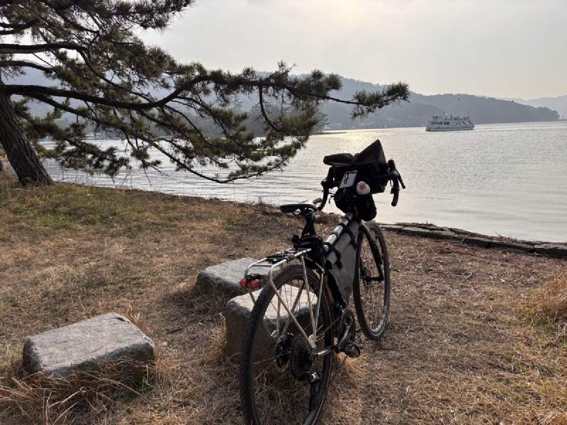 16:24,單車停在石頭旁,後面是海灣和一艘白色的船。