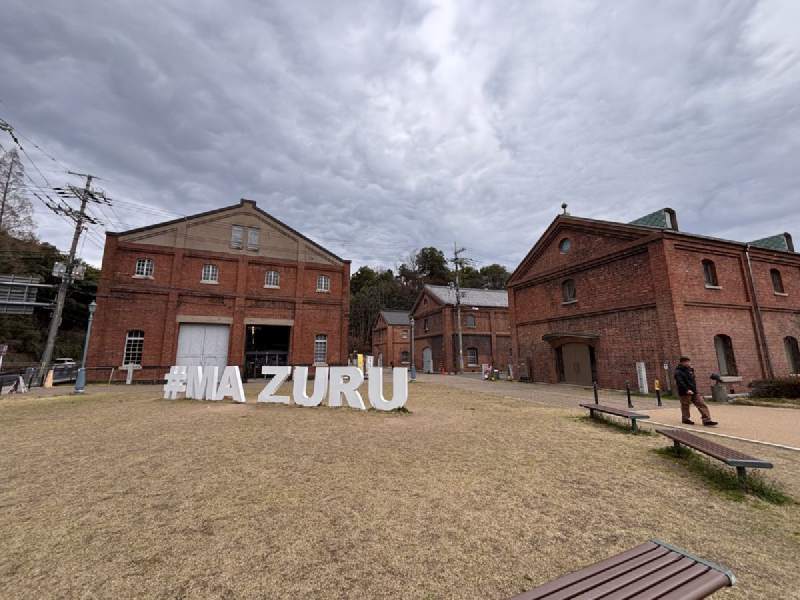 13:32,紅磚的老倉庫,前面的草地上立著「#MAIZURU」的白色大字。