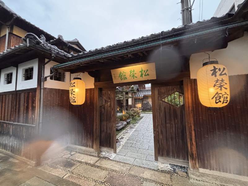 17:34,木造旅館的入口,燈籠上寫著「松榮館」,門裡是石板路。