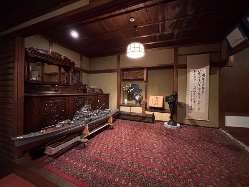 18:11,紅地毯的和室,櫃子上擺著一艘軍艦模型,旁邊掛著書法。