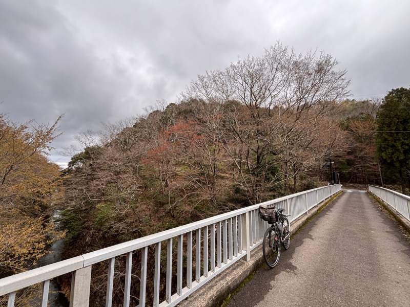 14:19,白色的橋欄杆,橋上靠著一台單車,後面是山丘。