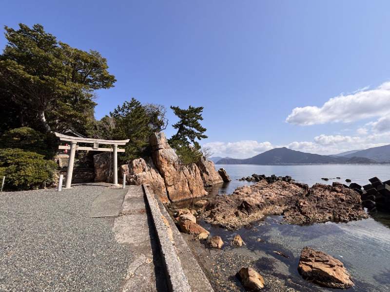 10:10,石板路通向海邊礁岩上的鳥居,旁邊是松樹。