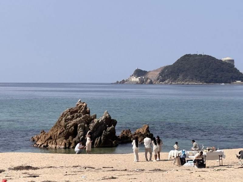 13:33,沙灘上一座礁岩,旁邊有幾個人,遠處是一座島。