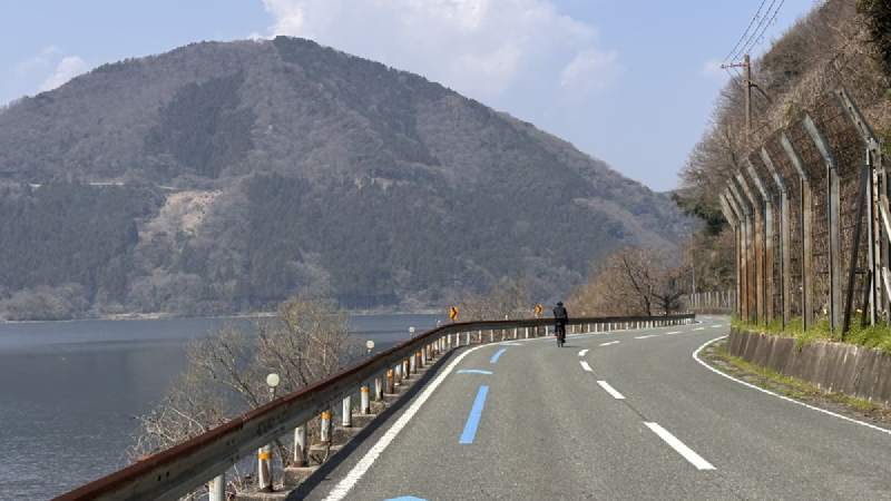 11:30,湖邊的彎路,地上有藍色的自行車路線標示,遠處是一座山。