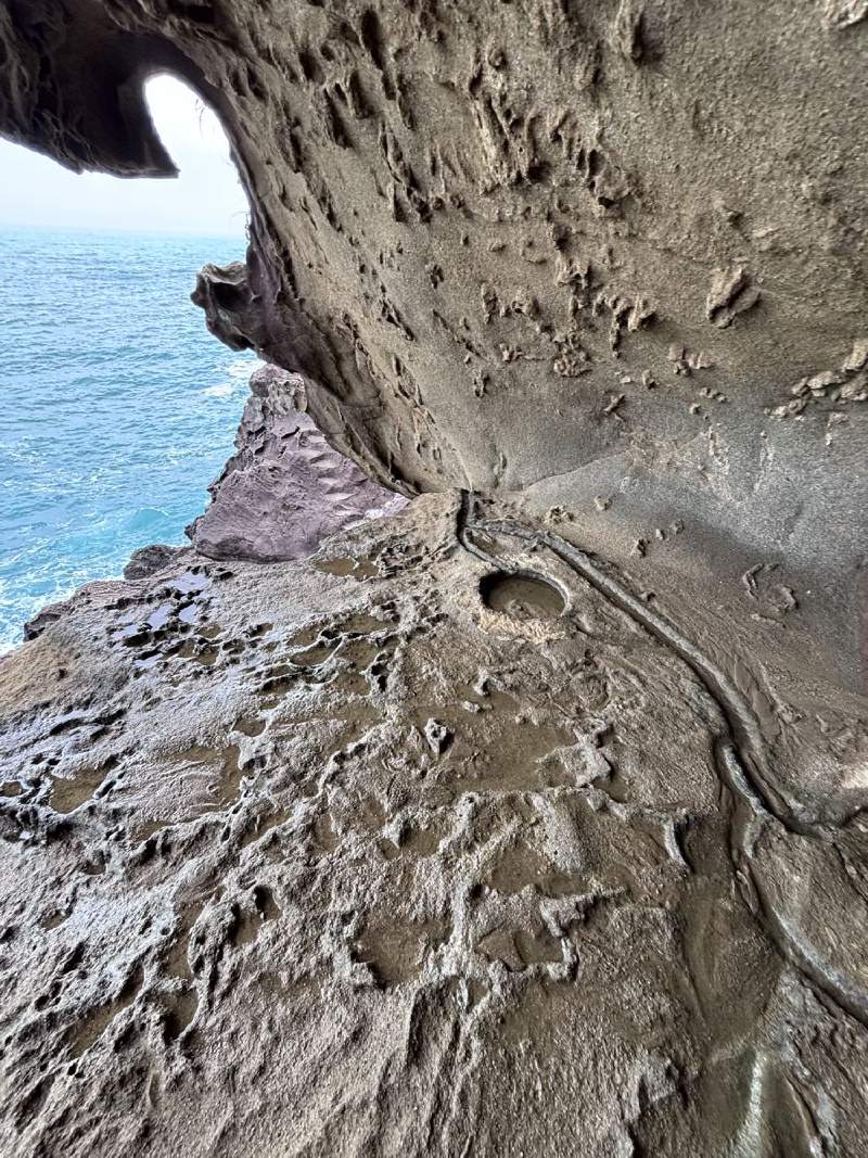 岩面坑坑洞洞,像被時間一口一口咬過;縫隙外,是湛藍的海。