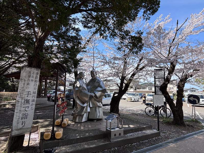 13:19,穗高神社的道祖神像,一對老夫婦手牽著手;櫻花正開,我的車停在後面。